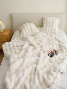 a bed covered in white fluffy blankets with a cup of coffee on the end table