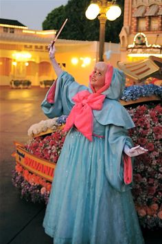 an old woman dressed in blue and pink holding a wand next to a flower bed