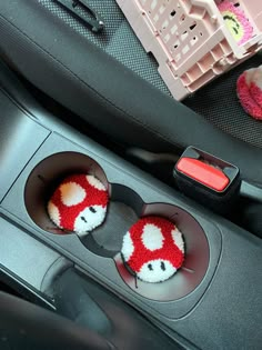 two cup holders in the center console of a car with red and white knitted mushrooms