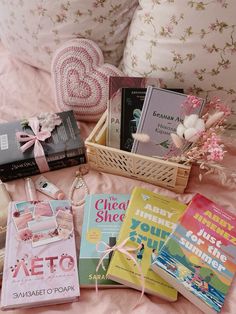 some books are laying on a bed next to a pink pillow and flower bouquets