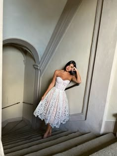 a woman in a white dress is standing on the stairs talking on her cell phone