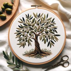 an embroidery project with olives and scissors on a white cloth next to a wooden cutting board