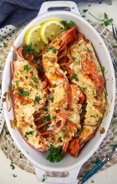 cooked lobster in a white dish with lemon wedges and parsley