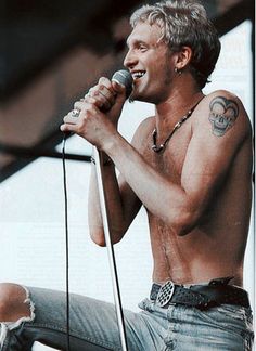 a man with no shirt on holding a microphone in his right hand and singing into the mic