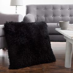 a black fluffy pillow sitting on top of a wooden floor next to a white table