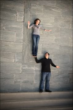 two people standing in front of a wall with their hands out and one person leaning up against the wall