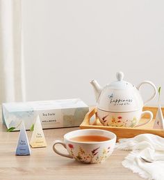 a tea pot and cup on a wooden tray next to two boxes of soaps