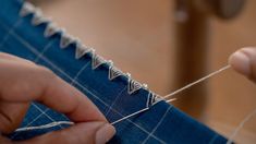 someone is stitching something on a blue piece of fabric with silver pins and thread