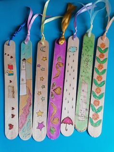 five wooden bookmarks with designs on them hanging from ribbons and tags attached to strings