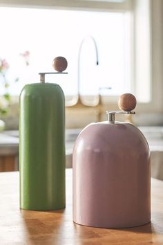 two green and pink vases sitting on top of a wooden table next to each other