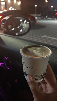 a hand holding up a cup of coffee in front of a car window at night