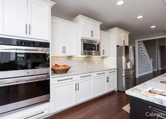 a large kitchen with white cabinets and stainless steel appliances, along with wood flooring