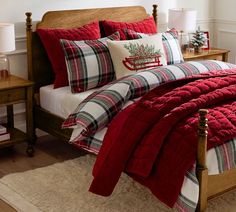 a bed with plaid comforter and pillows in a bedroom next to a christmas tree