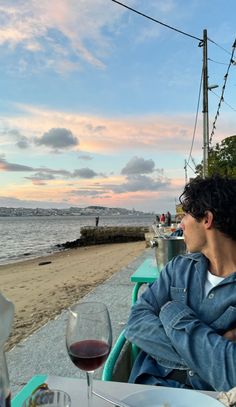 a man sitting at a table with a glass of wine in front of him on the beach