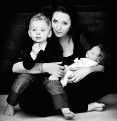 a woman sitting on the floor with two children in her lap and one holding a baby