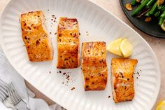 four pieces of salmon on a plate with asparagus and lemon wedges next to it