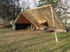 a wooden structure sitting on top of a lush green field next to a forest filled with trees