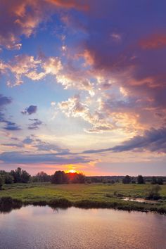 the sun is setting over a river with grass and trees in the background stock photo