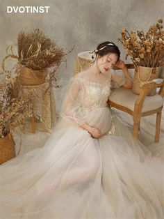 a woman in a white dress sitting on a chair next to dried flowers and plants