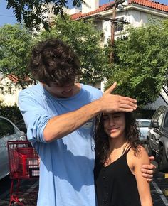 a man and woman standing next to each other in front of a parking lot with cars