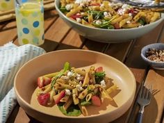 two bowls filled with pasta salad on top of a wooden table next to a glass of water