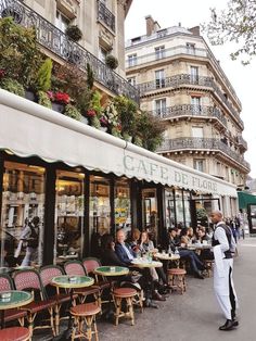 people sitting at tables in front of a cafe on a street with many windows and balconies