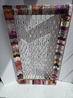 a piece of art that is made out of different colored fabrics and beads on a white surface