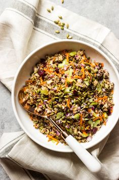 a white bowl filled with rice and veggies next to a silver serving spoon