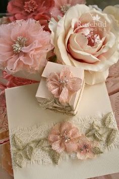 some pink flowers are sitting on top of a white piece of paper with lace and pearls