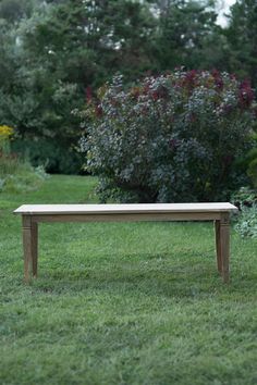 a wooden bench sitting in the middle of a lush green field next to trees and bushes