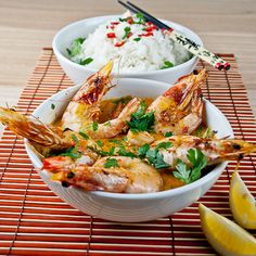 two bowls filled with shrimp and rice next to lemon wedges on a place mat