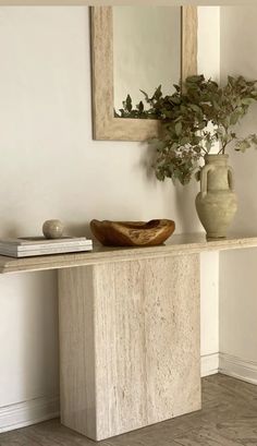 a table with a vase, mirror and books on it next to a plant in a vase