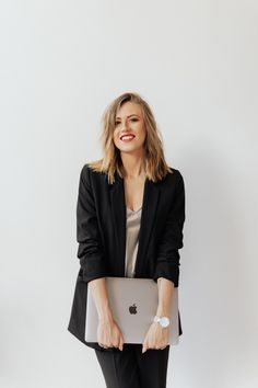 a woman holding an apple laptop computer in her hands while standing against a white wall