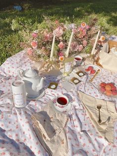 an outdoor picnic with tea and fruit on the table in the grass, next to some pink flowers