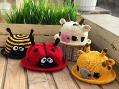 three crocheted hats sitting on top of a wooden table next to grass and flowers