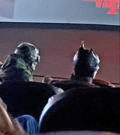 two people sitting in front of a projector screen with masks on their heads and one person wearing a batman mask