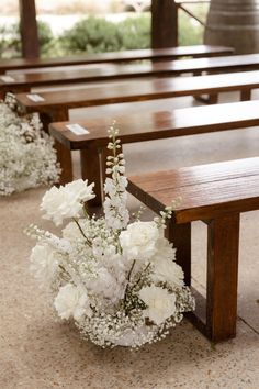 white flowers in a vase sitting on top of a wooden bench next to two pews