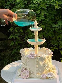 someone is pouring blue liquid on top of a white cake with pink flowers and roses