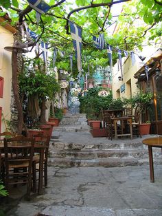 an alley way with tables and chairs on the steps leading up to some restaurants in greece