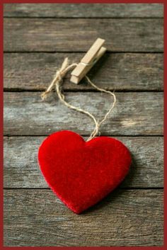 a red heart hanging from a string on top of a wooden table next to a pair of scissors