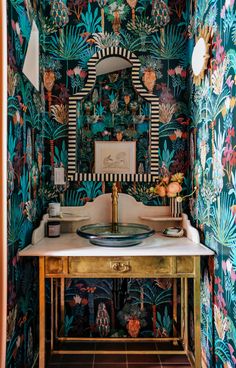 a bathroom with colorful wallpaper and a mirror on the sink area, surrounded by gold pedestals