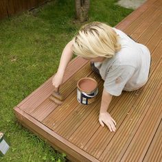 a woman is painting a wooden deck with a paintbrush and a can on the ground