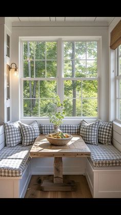 a wooden table sitting under a window next to a bench with pillows on top of it