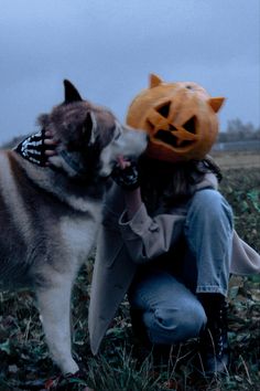 a woman kneeling down next to a dog with a pumpkin on it's head