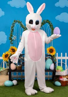 a man in bunny suit holding an egg next to sunflowers and other decorations