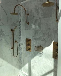 a bathroom with marble walls and gold shower faucets on the wall, along with two hand held shower heads