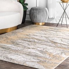 a white and gold rug in a living room next to a couch with a vase on the floor