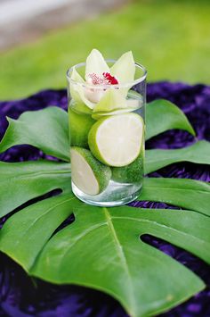 a glass filled with water sitting on top of a green leaf covered table next to a flower