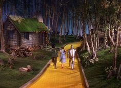 two people walking down a yellow path in front of a small wooden cabin with green roof