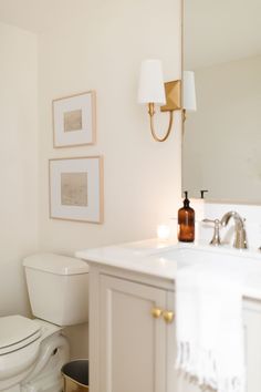 a white toilet sitting next to a sink in a bathroom under two pictures on the wall